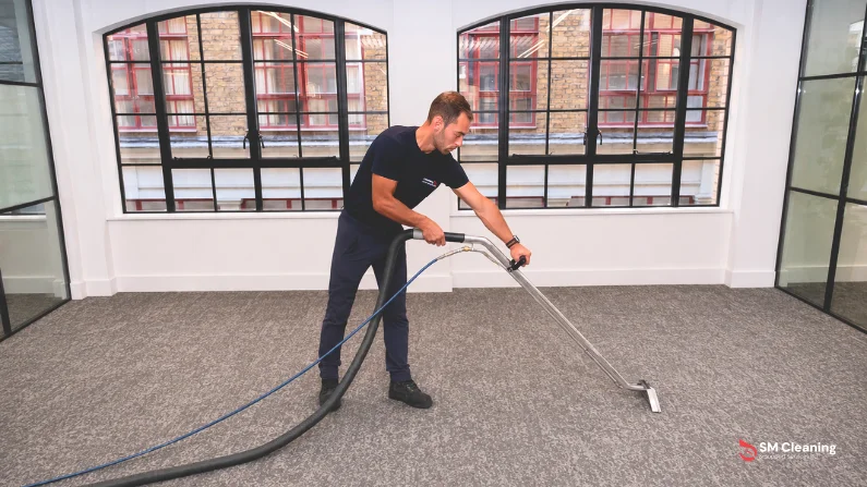 SM Cleaning operative professionally cleaning a grey office carpet using commercial carpet extraction equipment in a London office.